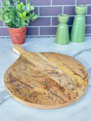 a round mango wood cheese and cutting board with etched flowers