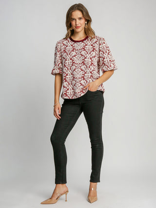 a boxy red knit jacquard top with a round neck and elegant pattern with fun puff sleeves worn with black jeans