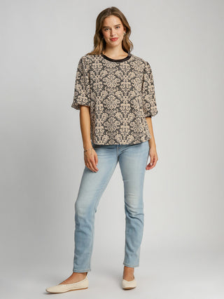 a boxy black knit jacquard top with a round neck and elegant pattern with fun puff sleeves worn with light blue jeans