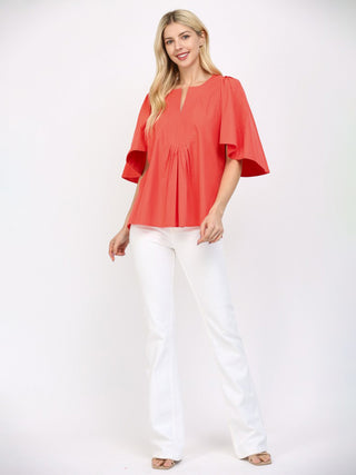 a flattering coral orange cinched blouse with short flutter sleeves worn with white pants