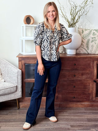 a billowy navy paisley print split neck top with short puff sleeves worn with dark denim pants