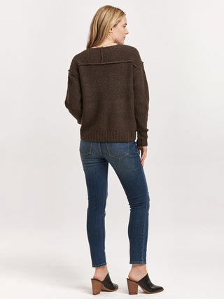 long sleeve brown knit sweater with drop shoulders and exposed seams worn with dark blue denim jeans