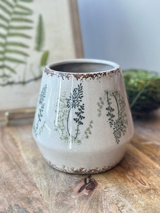 a white and cream ceramic pot with a fresh green fern pattern