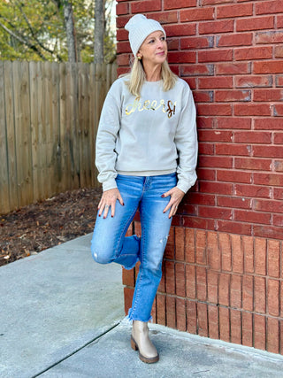 a sand colored crewneck sweatshirt with a golden cheers emblem worn with jeans