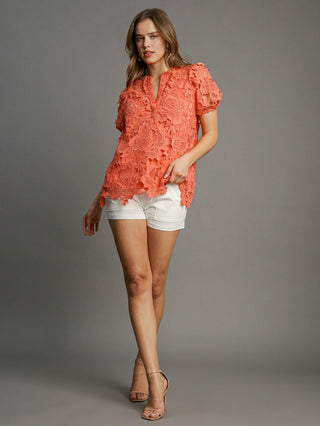 a lacy coral orange top with puff sleeves and a split neckline worn with white shorts