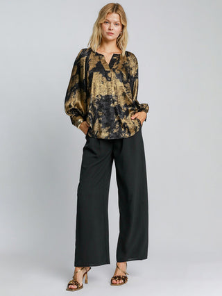 a soft elegant gold metallic v neck blouse with a night time abstract print worn with black pants