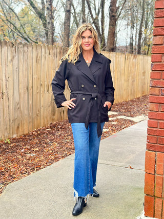 a classy and warm short black trench coat with golden button closures worn with blue jeans and black boots