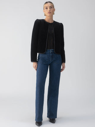 a simple black quilted velvet jacket with a snap closure worn with jeans