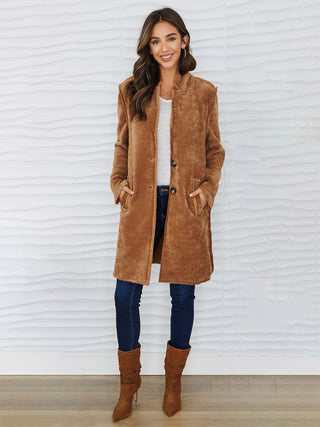 a long trendy camel colored button front corduroy jacket worn with jeans and brown boots