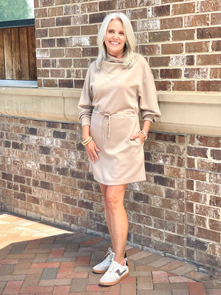 a cozy taupe sweater dress with a high crowl neck and adjustable waist tie worn with white sneakers