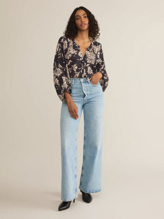 a flowy purple and cream floral print blouse with front buttons and long billowy sleeves worn with light denim