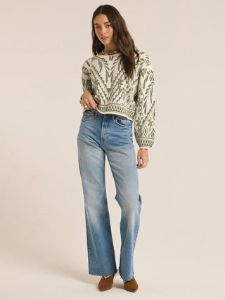 a cozy long sleeve crew neck sweater with a green palm print pattern worn with washed jeans